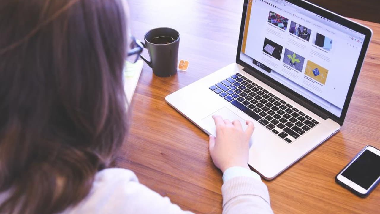 Woman working on a laptop at a wooden desk with a cup of coffee